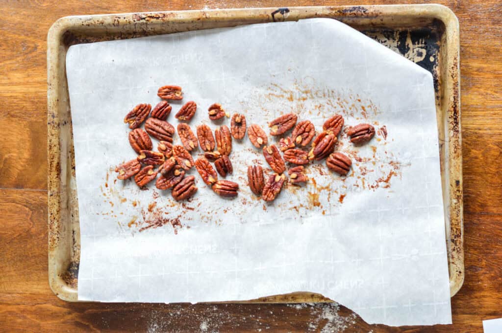 Looking down on a sheet pan topped with parchment paper and roasted pecans out of the oven
