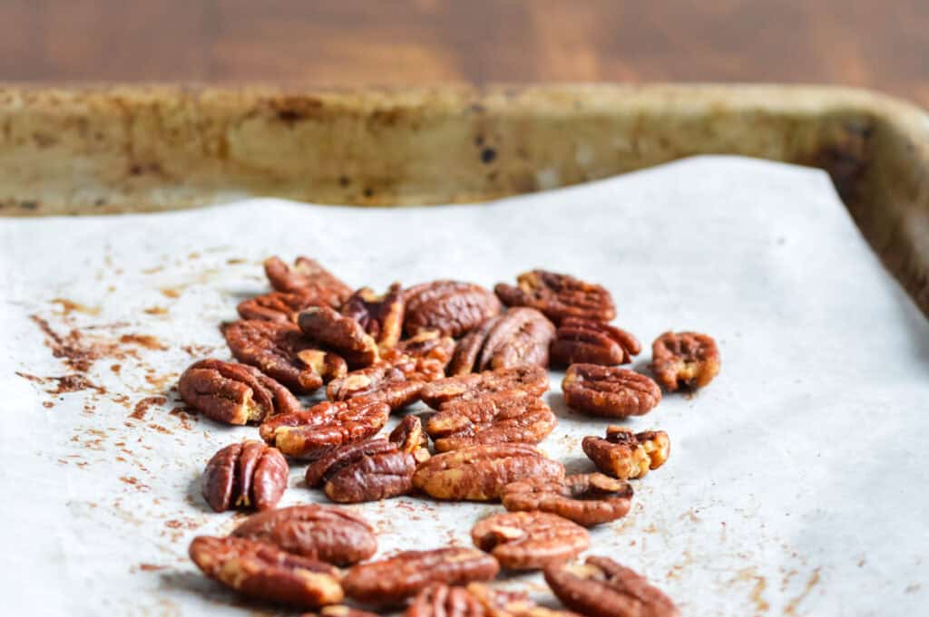 Side view of roasted pecans on parchment paper and baking sheet
